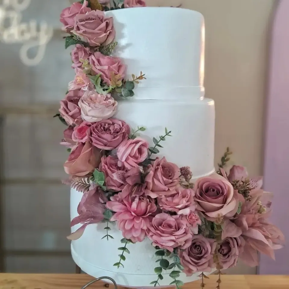 Bolo fake branco com uma cascata de flores em tons de rosa e folhagens verdes
