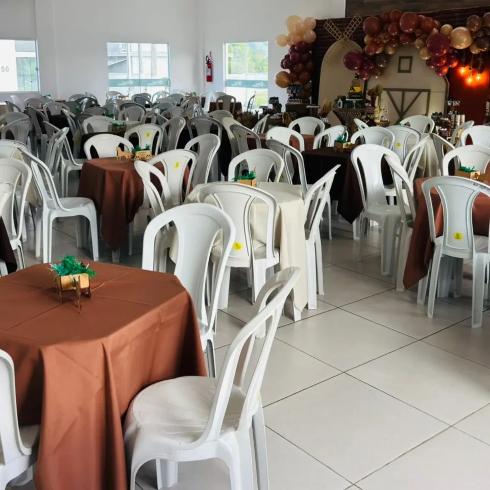 Salão de festa com mesas cobertas por toalhas marrons e cadeiras brancas
