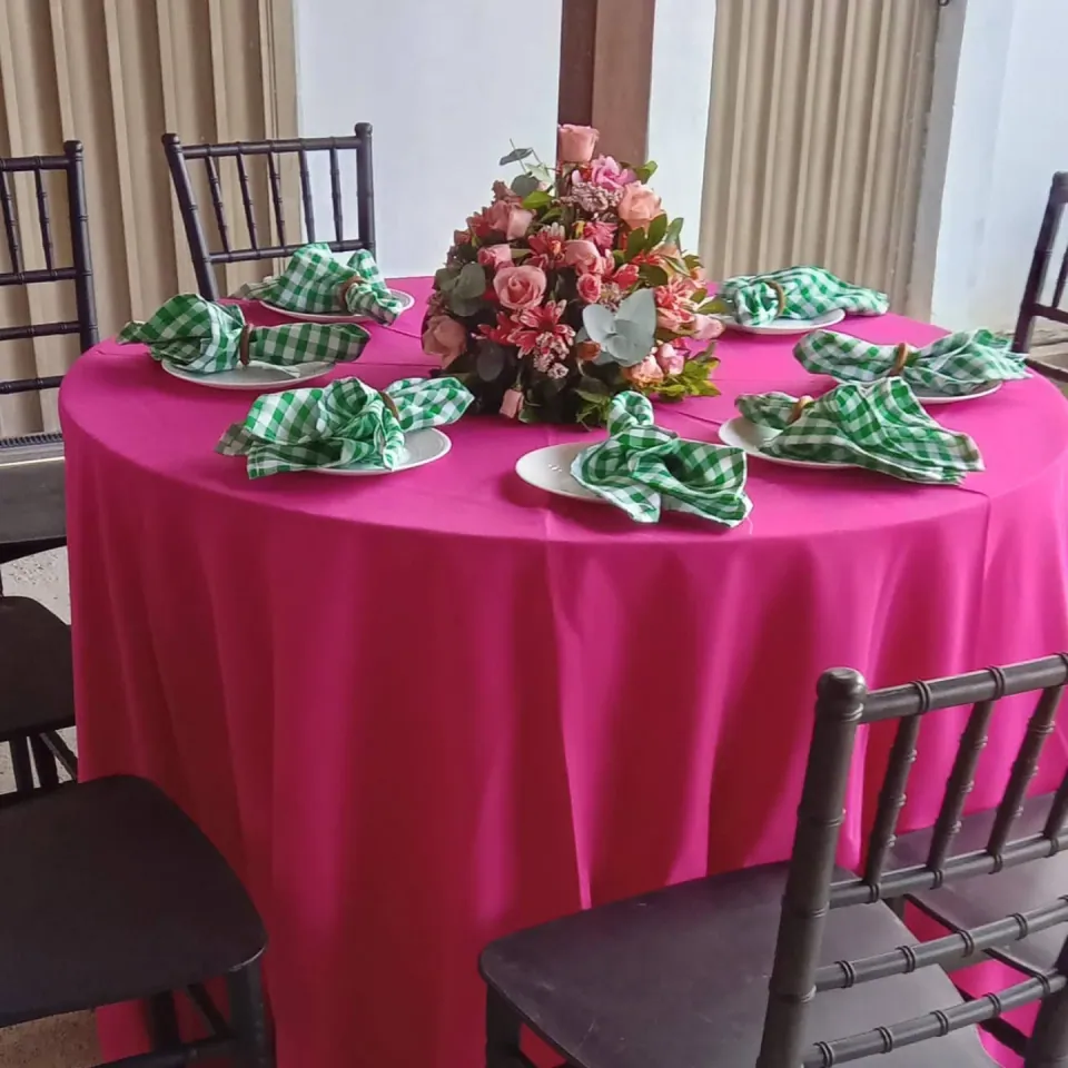 Mesa de festa com toalha rosa, arranjo de flores, pratos brancos e guardanapos verdes
